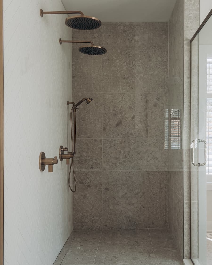 Stone-tiled walk-in shower with dual rainfall heads and bronze fixtures